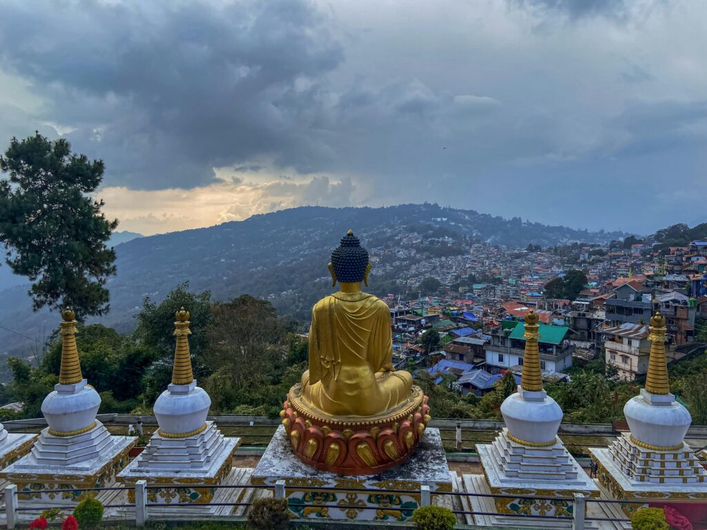 A serene golden Buddha statue with Kalimpong's lush landscape in the background, captured at sunset.